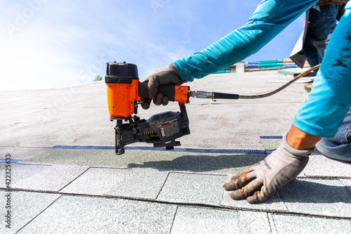 roofer installing roof shingles with nail gun photo