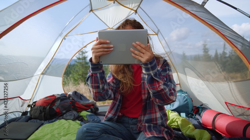 Girl talking online on video chat at digital tablet in tent. Tourist using pad