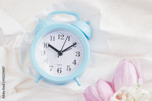 blue alarm clock, flowers on bed, spring morning mood concept photo