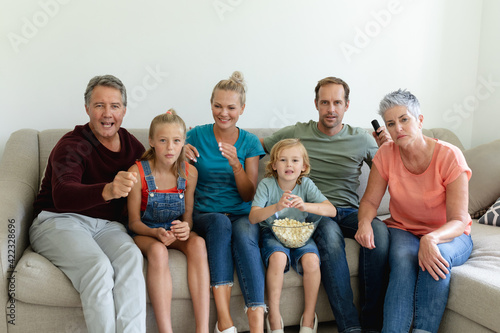 Caucasian parents, grandparents and grandchildren sitting on couch watching tv