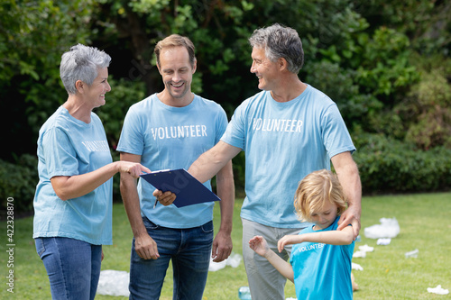 Caucasian senior couple with clipboard and man and son in volunteer shirts talking in littered field