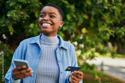 Young african american woman smiling happy holding smartphone and credit card at the city