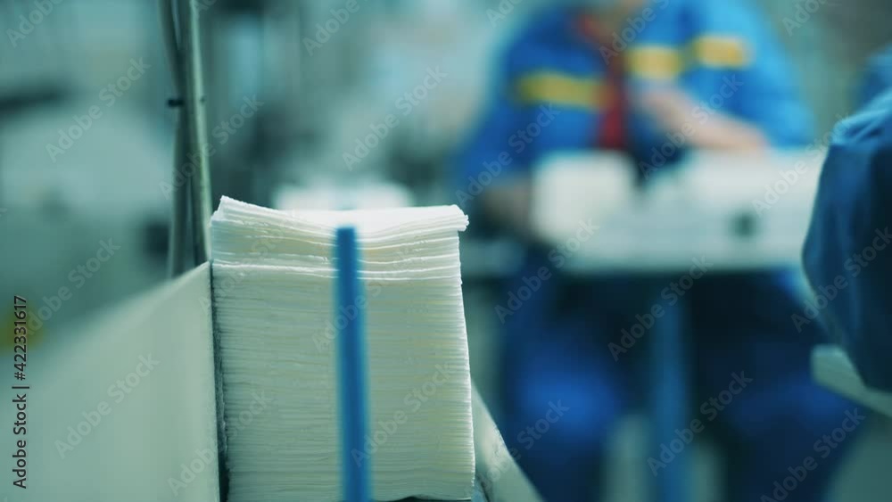 Worker stacking paper tissues on a conveyor belt at a paper mill Worker stacking paper tissues on a conveyor belt at a paper mill