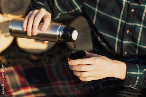 Traveler man pouring hot coffee from thermos, outdoors. Hiking and travel. Close up, cropped shot.