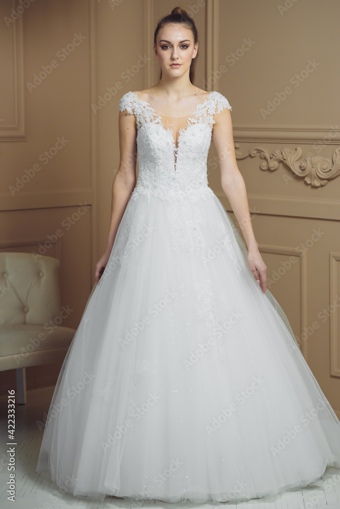 Beautiful attractive bride in wedding dress with long full skirt, beige background Beautiful attractive bride in wedding dress with long full skirt, beige background