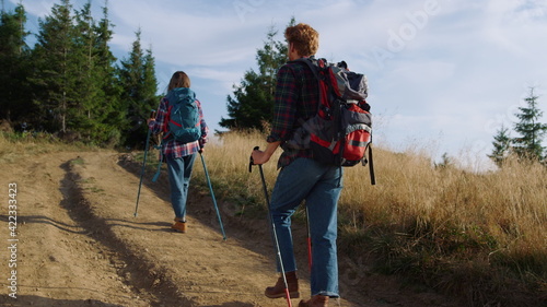 Serious man and woman trekking on road in mountains. Tourists using hiking poles