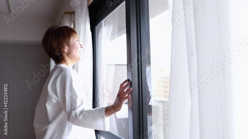 窓を開けて外を眺める日本人ミドル女性