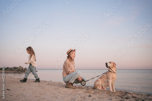 Young mother and daughter walk with dog on the beach