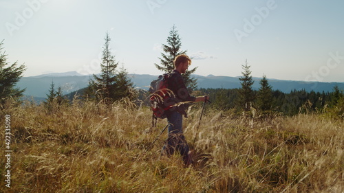 Man walking on mountain road with backpack. Serious guy using trekking poles