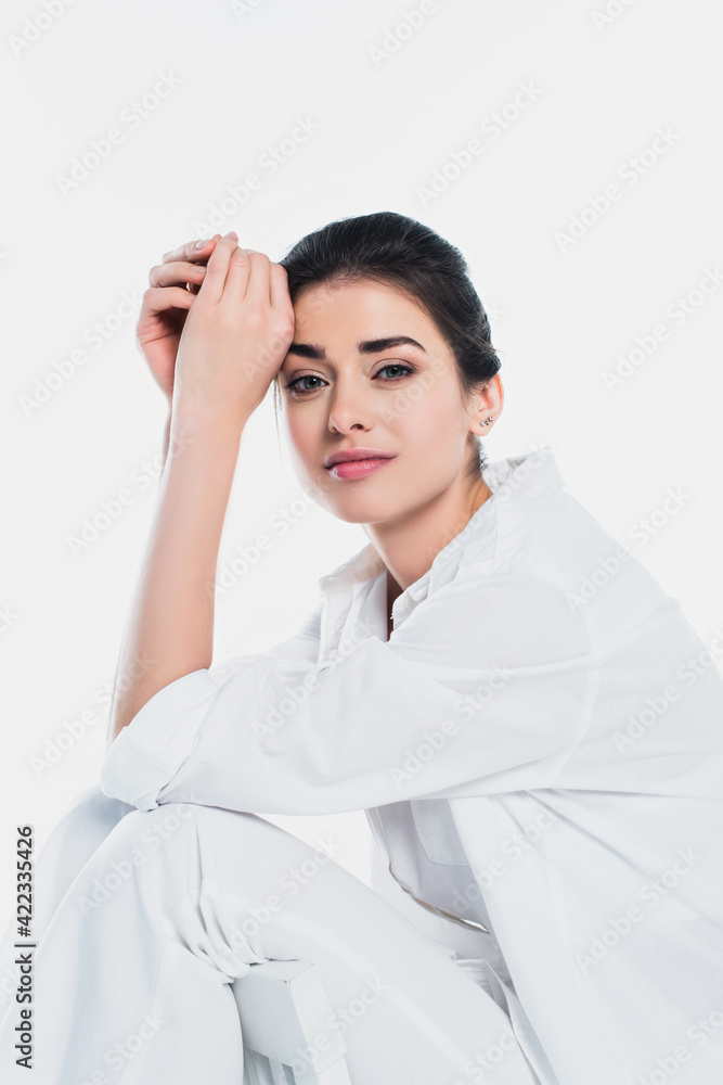 Brunette woman in shirt looking at camera on chair isolated on white Brunette woman in shirt looking at camera on chair isolated on white