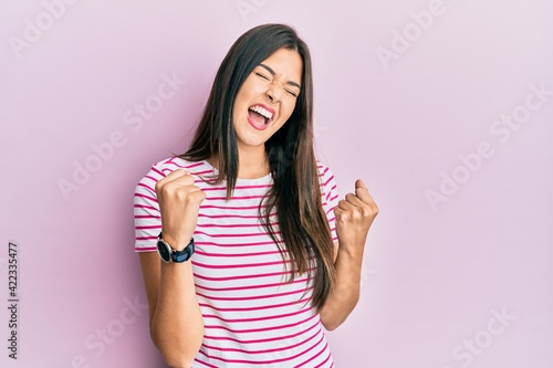 Young brunette woman wearing casual clothes over pink background celebrating surprised and amazed for success with arms raised and eyes closed. winner concept.