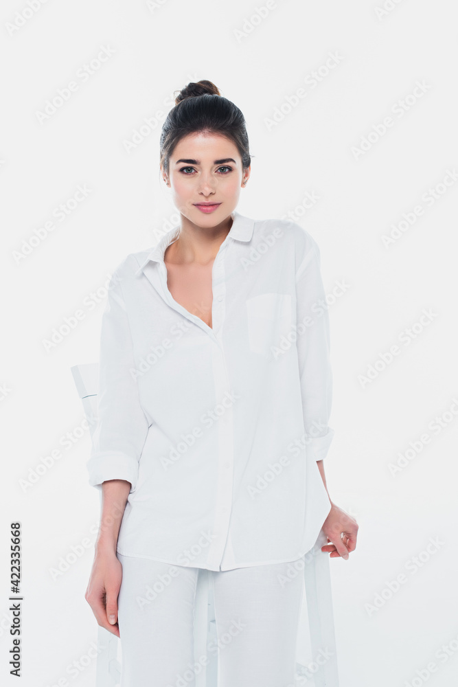 Pretty woman in white shirt looking at camera near chair isolated on white Pretty woman in white shirt looking at camera near chair isolated on white