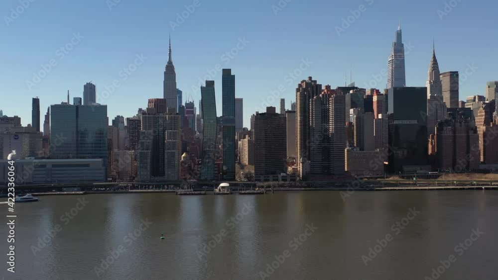 An aerial view over a calm East River on a sunny day with blue skies. The drone camera facing midtown Manhattan, dolly in towards the Empire State Building. An aerial view over a calm East River on a sunny day with blue skies. The drone camera facing midtown Manhattan, dolly in towards the Empire State Building.