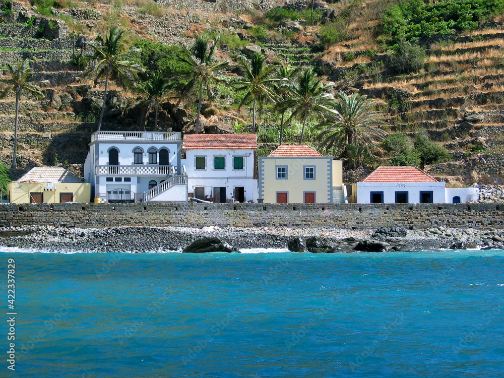 Waterfront homes on a tropical island, Brava island, Cabo Verde, blue ocean water, stony beach and terraced fields on the hills.