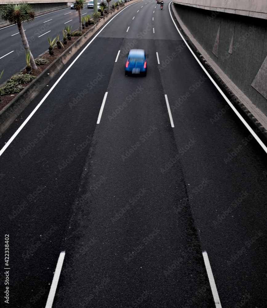 A blue car in movement on a black asplalt road, light trails and intentional movement/zoom effect.