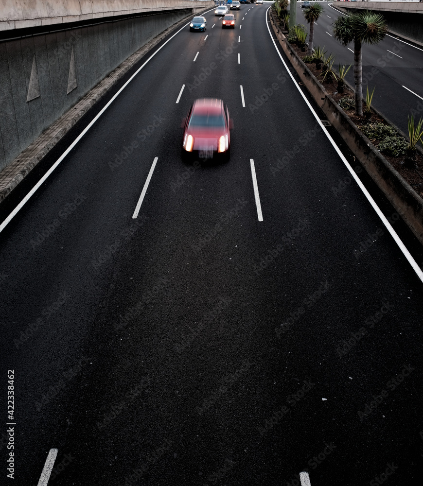 A red car in movement on a black asplalt road, light trails and intentional movement/zoom effect.