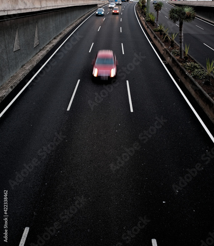 A red car in movement on a black asplalt road, light trails and intentional movement/zoom effect.