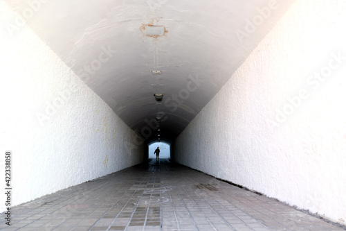 Small human figure disappearing in dark end of a light tunnel.