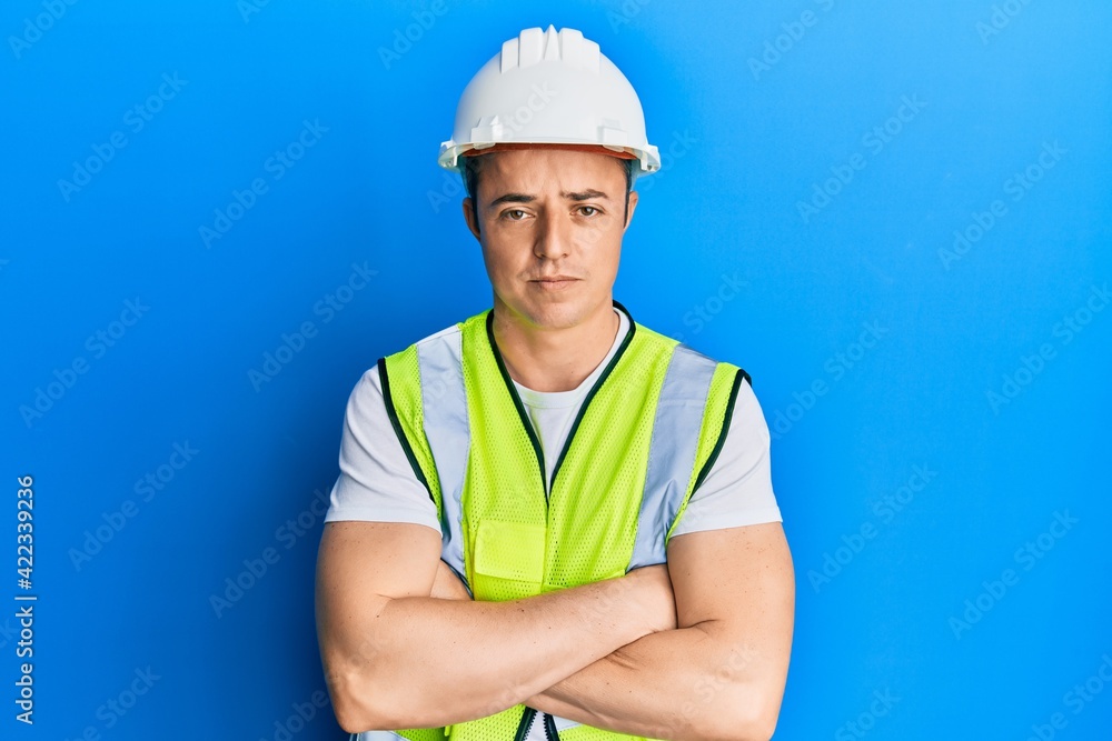 Handsome young man wearing safety helmet and reflective jacket skeptic and nervous, disapproving expression on face with crossed arms. negative person. Handsome young man wearing safety helmet and reflective jacket skeptic and nervous, disapproving expression on face with crossed arms. negative person.