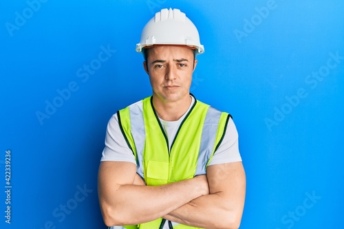 Handsome young man wearing safety helmet and reflective jacket skeptic and nervous  disapproving expression on face with crossed arms. negative person.