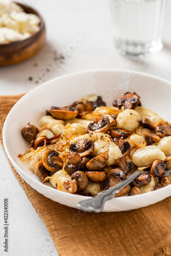 Gnocchi with mushrooms close-up. Cooked potato gnocchi with fried champignons and onions in a white plate on a light concrete table. Italian cuisine.