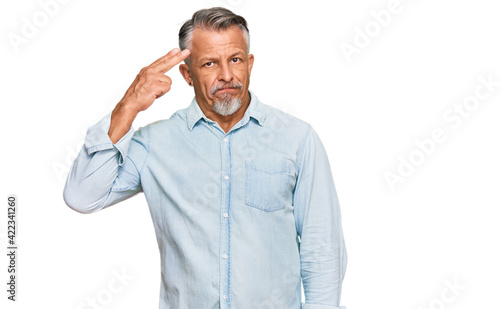 Middle age grey-haired man wearing casual clothes shooting and killing oneself pointing hand and fingers to head like gun, suicide gesture.
