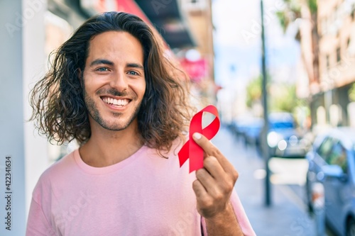 Photos Young hispanic man smiling happy holding hiv awareness red ribbon at city