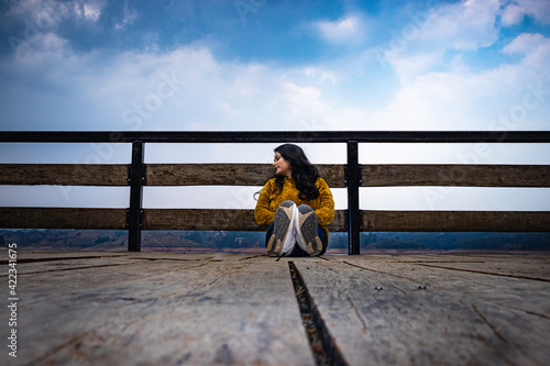 young girl sitting at wood bridge with cloudy sky from low angle leading line and space for text