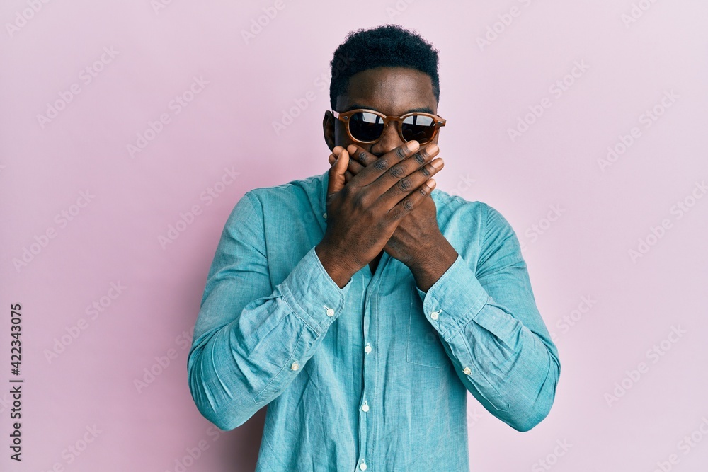 Handsome business black man wearing stylish sunglasses shocked covering mouth with hands for mistake. secret concept. Handsome business black man wearing stylish sunglasses shocked covering mouth with hands for mistake. secret concept.