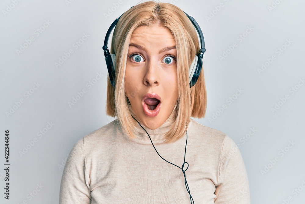Young blonde woman listening to music using headphones scared and ...