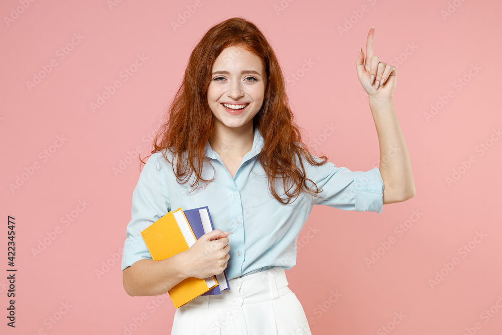 Young insighted proactive redhead student woman in blue shirt hold book index finger up great new idea isolated on pastel pink background studio portrait Education school university college concept. Young insighted proactive redhead student woman in blue shirt hold book index finger up great new idea isolated on pastel pink background studio portrait Education school university college concept.