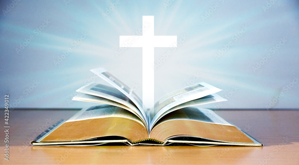 Naklejka premium Cross Crucifixion Of Jesus Christ Floating above the old book on the wooden table with greyish blue color background, Easter concept. narrow depth of field.