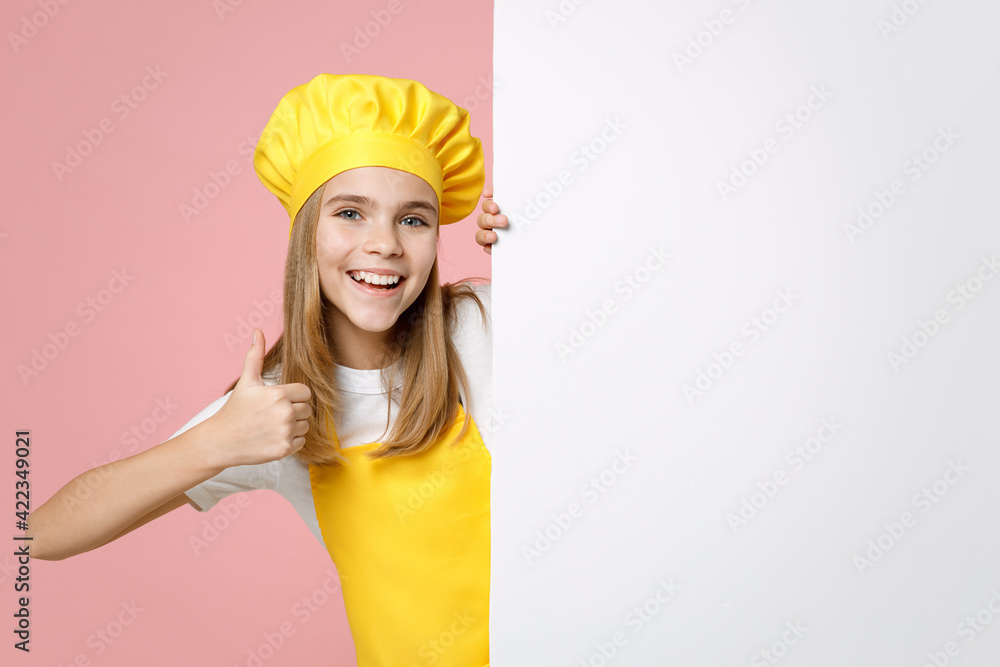 Teen girl chef cook confectioner housewife baker in yellow apron white t-shirt cap hold blank promotional content place board for text show thumb up gesture isolated on pink background Food concept. Teen girl chef cook confectioner housewife baker in yellow apron white t-shirt cap hold blank promotional content place board for text show thumb up gesture isolated on pink background Food concept.