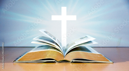 Cross Crucifixion Of Jesus Christ Floating above the old book on the wooden table with greyish blue color background, Easter concept. narrow depth of field. © masterjew