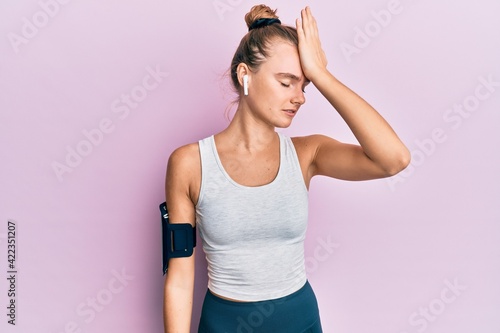 Beautiful blonde sport woman wearing arm band and earphones surprised with hand on head for mistake, remember error. forgot, bad memory concept. © Krakenimages.com
