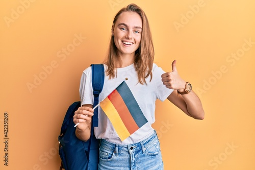Beautiful blonde woman exchange student holding germany flag smiling happy and positive  thumb up doing excellent and approval sign