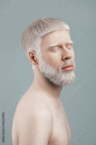Calm albino bearded guy with closed eyes posing against grey background in studio photo