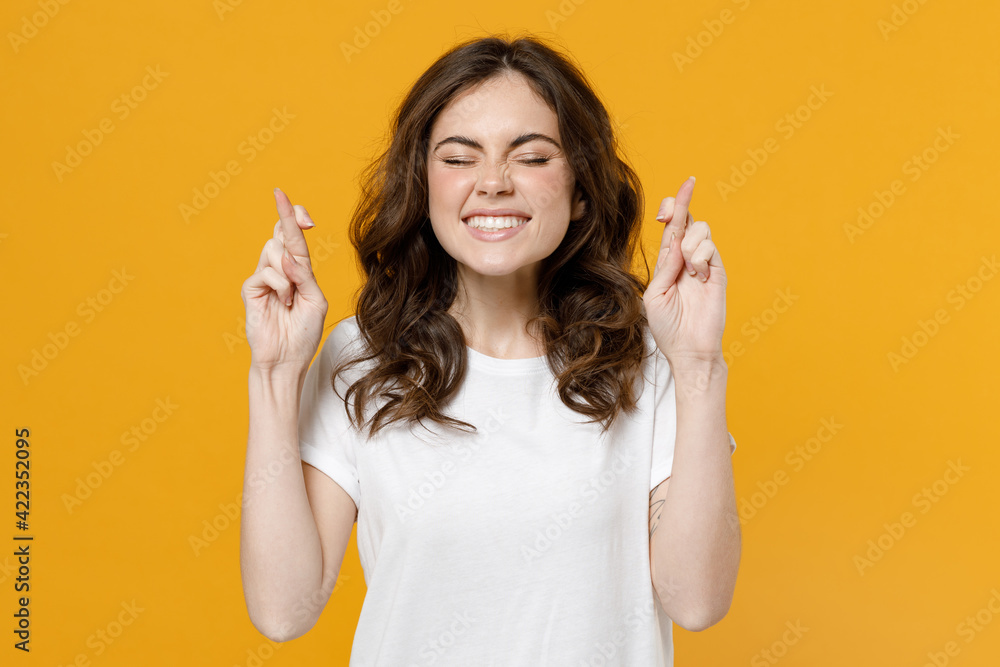 Young expectant caucasian woman 20s in white basic casual blank print design tshirt wait for special moment, keep fingers crossed making wish eyes closed isolated on yellow background studio portrait Young expectant caucasian woman 20s in white basic casual blank print design tshirt wait for special moment, keep fingers crossed making wish eyes closed isolated on yellow background studio portrait