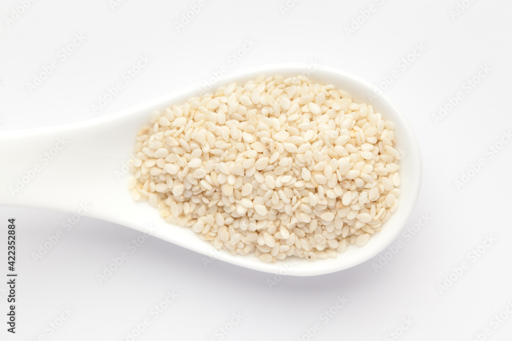 Macro Close up of Organic White Sesame seeds(Sesamum indicum) polished or white Til without the shell on a white ceramic soup spoon. Top view Macro Close up of Organic White Sesame seeds(Sesamum indicum) polished or white Til without the shell on a white ceramic soup spoon. Top view