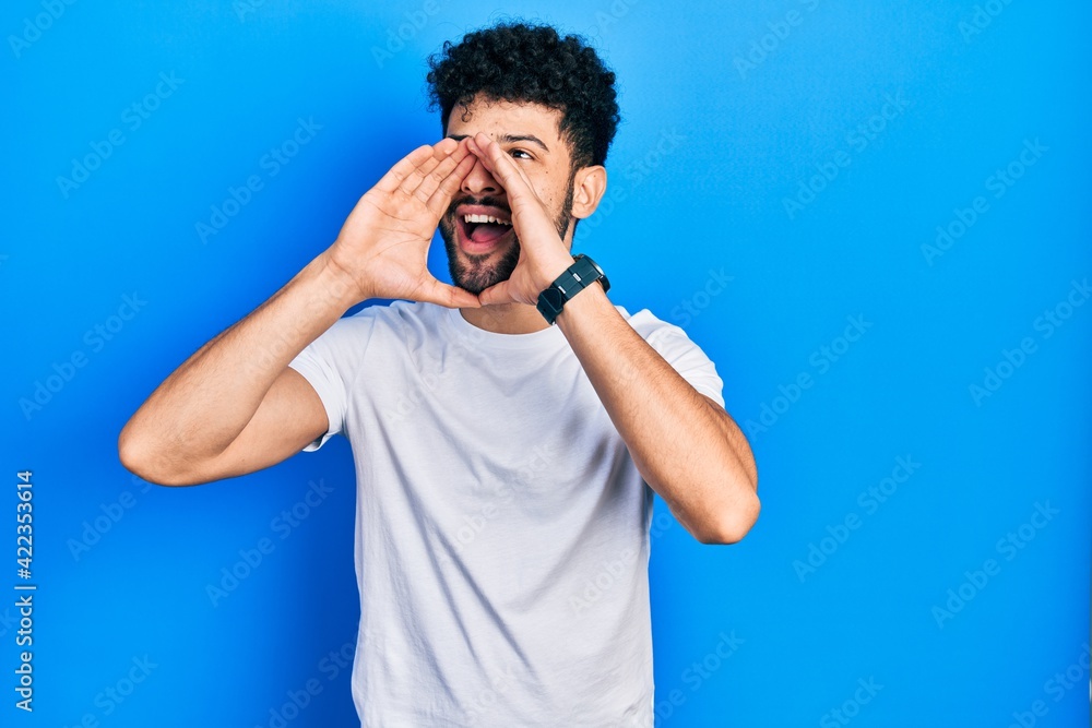 Young arab man with beard wearing casual white t shirt shouting angry out loud with hands over mouth Young arab man with beard wearing casual white t shirt shouting angry out loud with hands over mouth