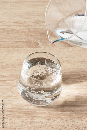 Pouring water from a jug into a glass on wooden background.