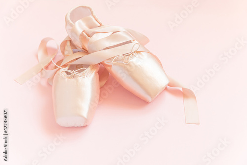 New pastel beige ballet shoes with satin ribbon isolated on pink background. Ballerina classical pointe shoes for dance training. Ballet school concept. Top view flat lay, copy space