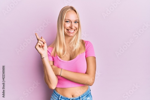 Young blonde girl wearing casual clothes with a big smile on face, pointing with hand and finger to the side looking at the camera. © Krakenimages.com