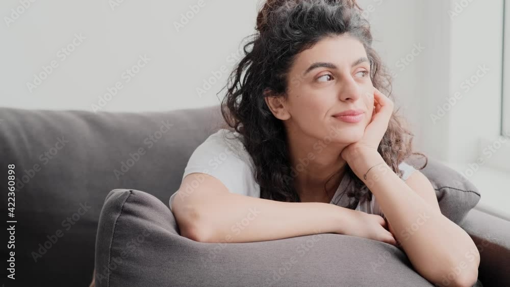 A beautiful young woman is sitting on the sofa and looking to the side at home A beautiful young woman is sitting on the sofa and looking to the side at home