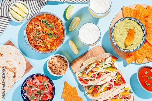 Mexican food table with traditional dishes. Chili con carne, tacos, tomato salsa, corn chips with guacamole. Mexican feast in hard light on blue color background, top view