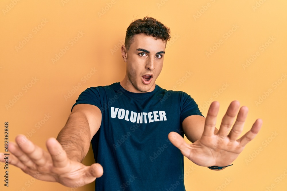 Hispanic young man wearing volunteer t shirt doing stop gesture with hands palms, angry and frustration expression Hispanic young man wearing volunteer t shirt doing stop gesture with hands palms, angry and frustration expression