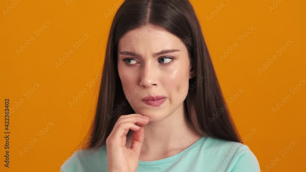 A displeased confused young woman is looking to the camera standing isolated over orange background in the studio A displeased confused young woman is looking to the camera standing isolated over orange background in the studio