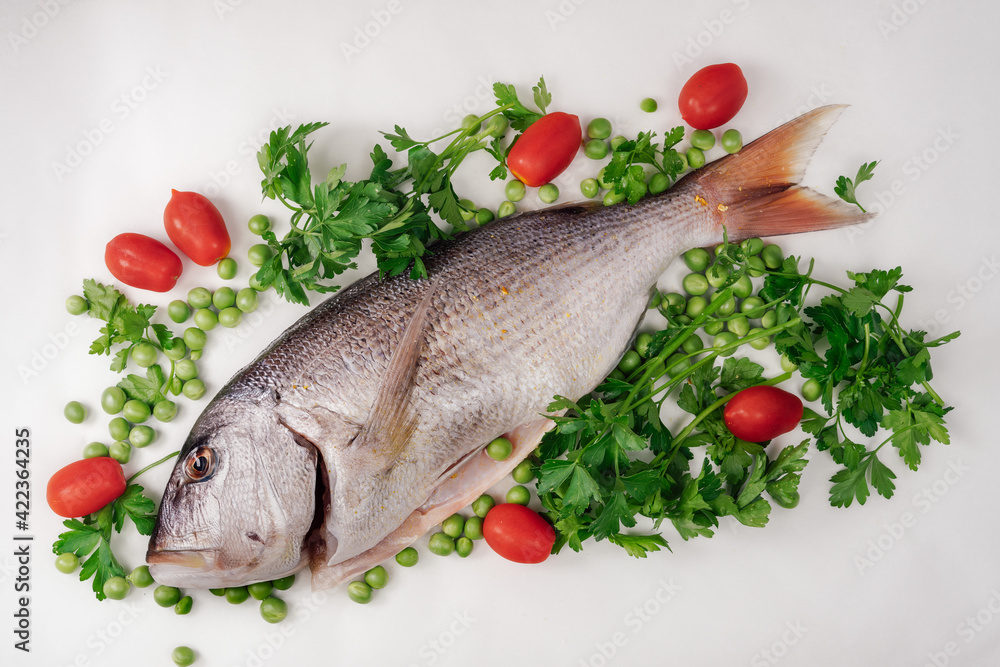 Whole dentex fish ready to cook top view, against white background. Close up of freshwater seafood, garnished with cherry tomatoes, fresh peas and parsley leaves on a flat surface. Whole dentex fish ready to cook top view, against white background. Close up of freshwater seafood, garnished with cherry tomatoes, fresh peas and parsley leaves on a flat surface.