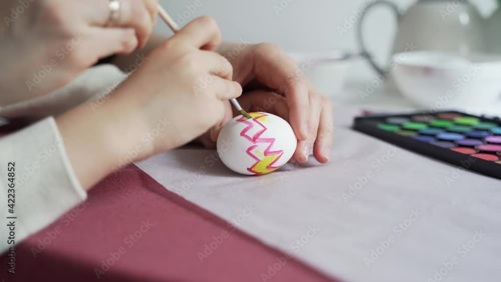Mom helps her little son to draw a pattern on an Easter egg Mom helps her little son to draw a pattern on an Easter egg