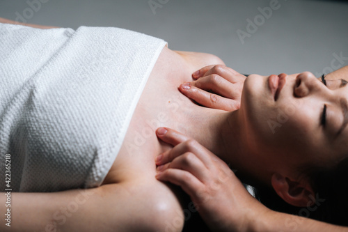 Close-up side view of young woman lying down on massage table with closed eyes during shoulder and neck massage at spa salon. Male masseur professionally massaging shoulders on black background.